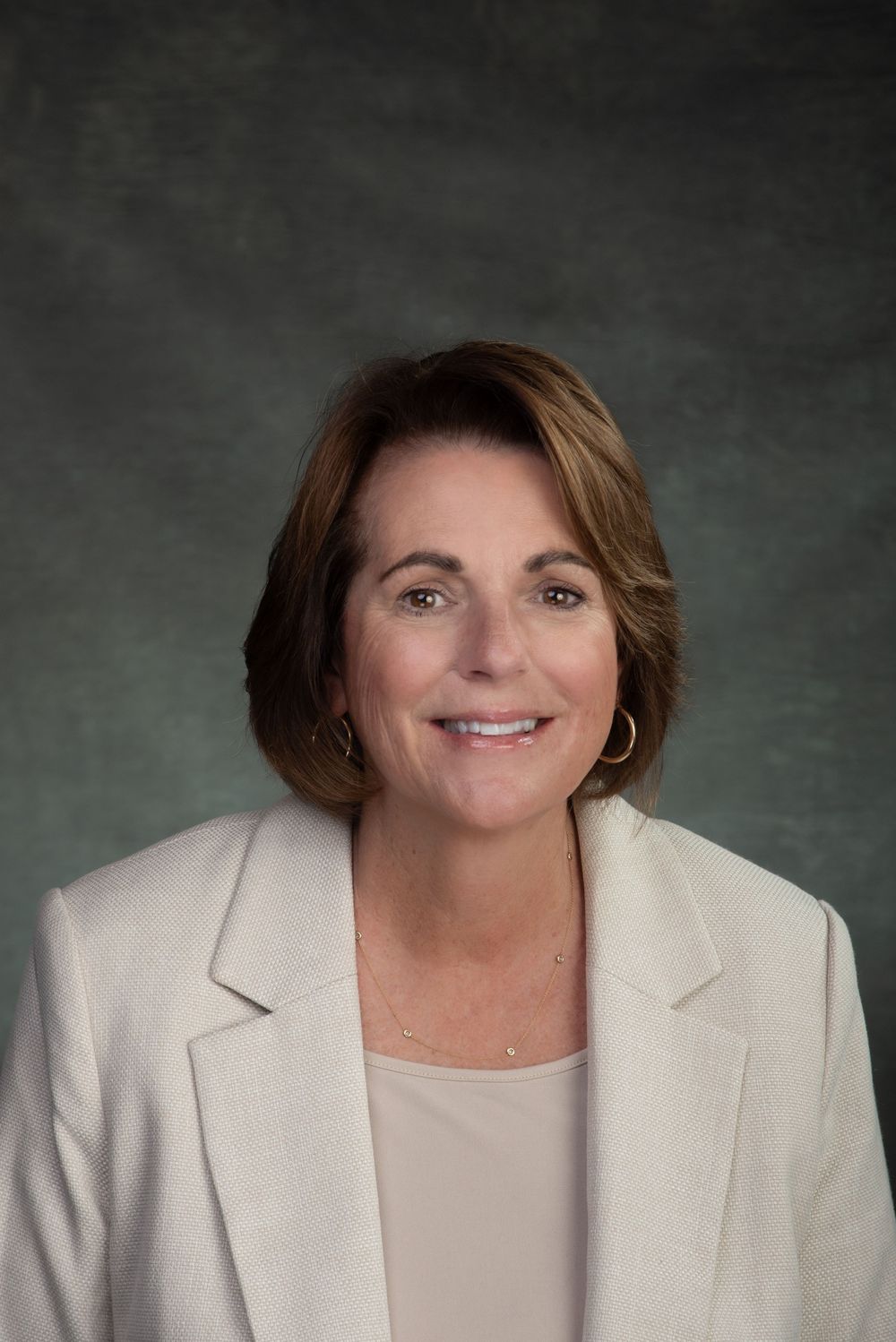Business headshot of woman in a white suit and shirt with short brown hair.