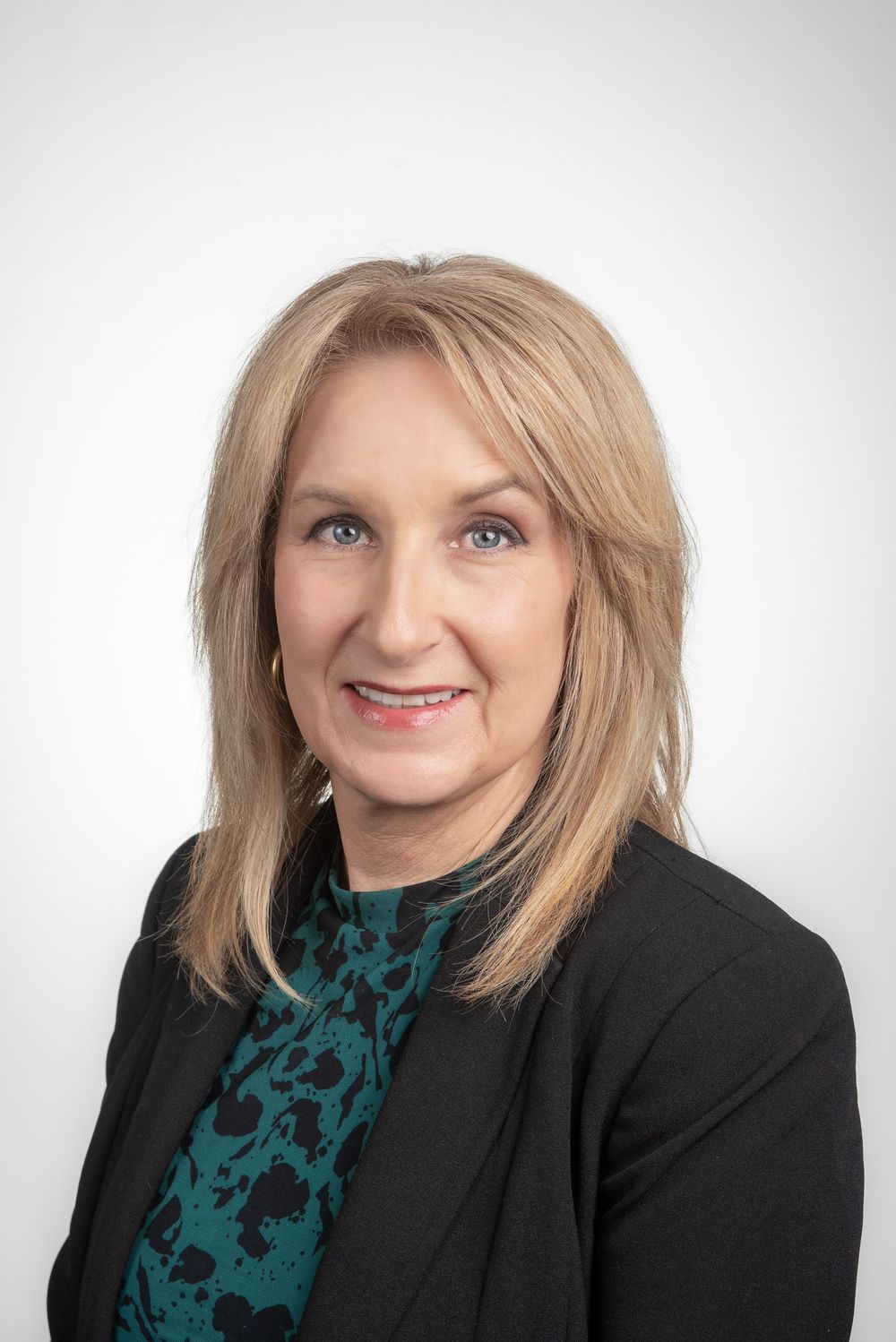 Business headshot of blonde woman in black suit jacket with white background.