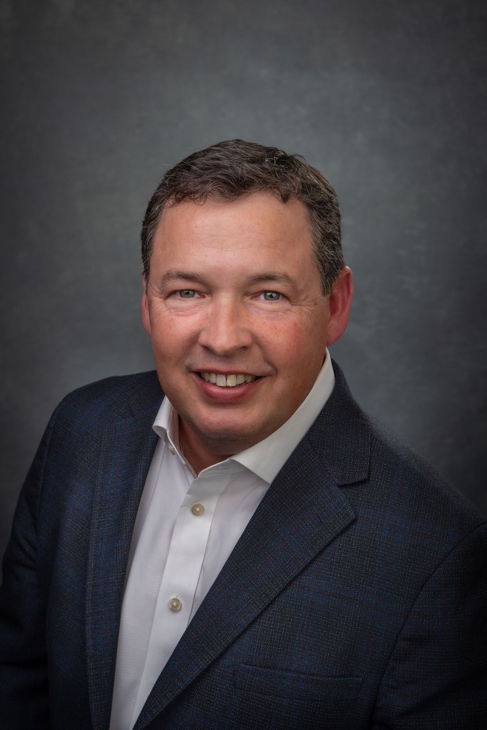 Business headshot of man in a blue suit with white shirt.