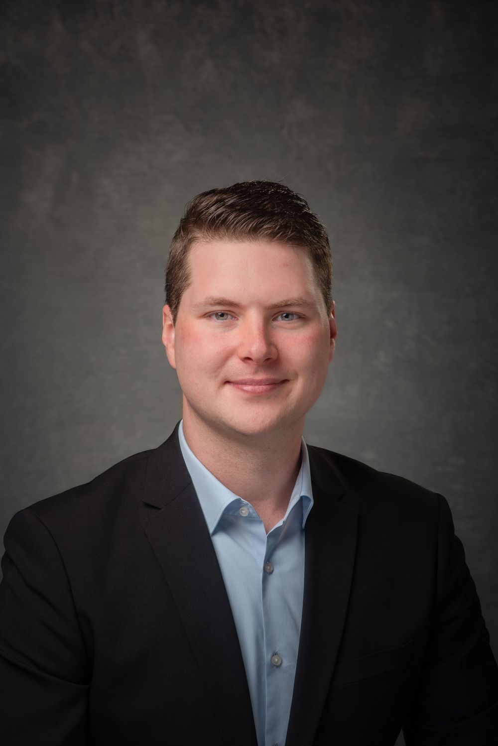 Business headshot of younger man in a suit and blue shirt.