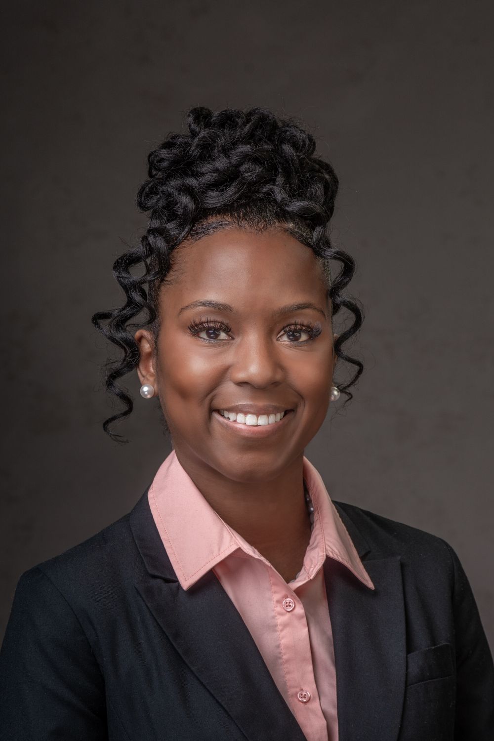 Headshot of black woman in black business suit with pink shirt and hair up.