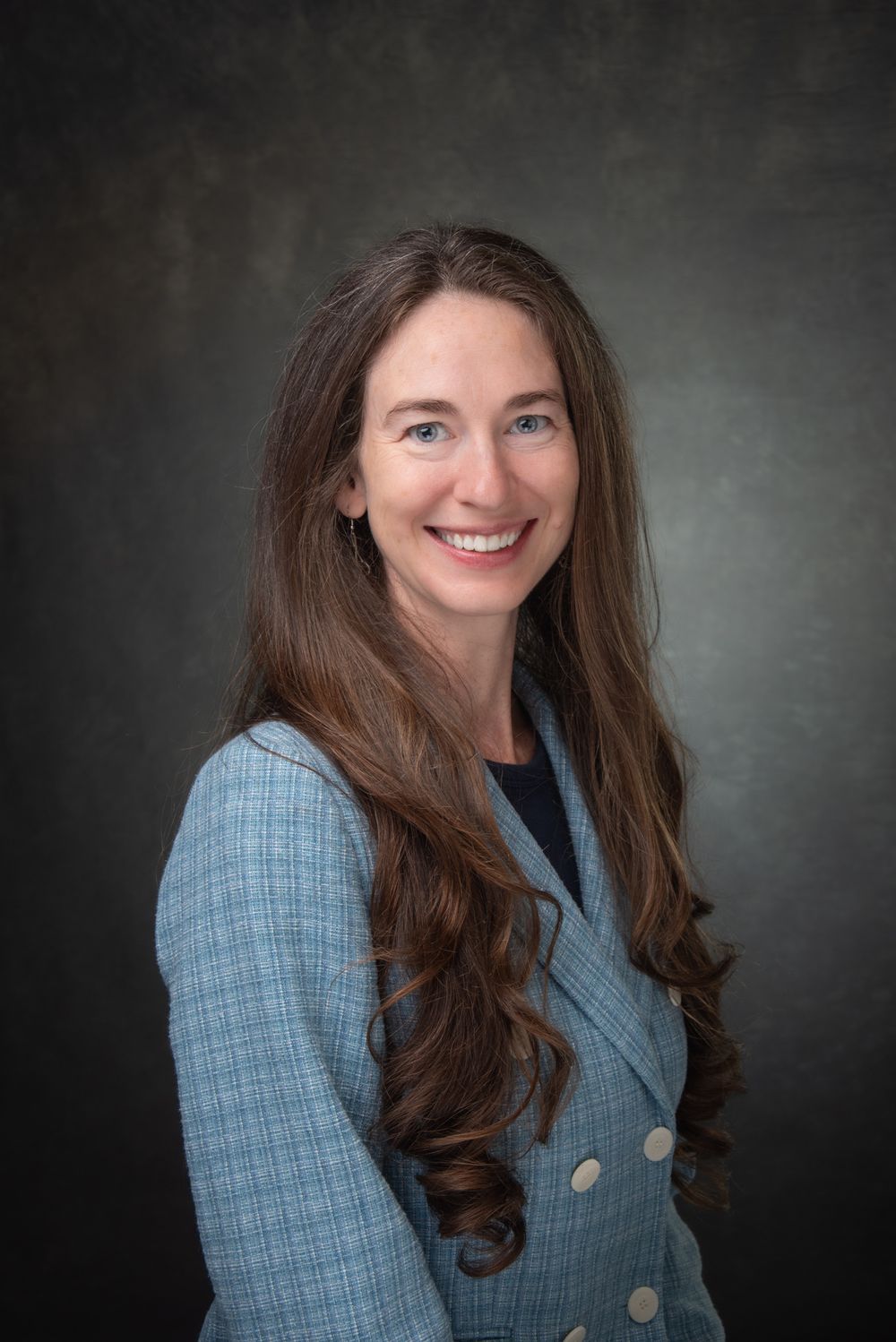 Business headshot of white lady with long brown hair and light blue suit.