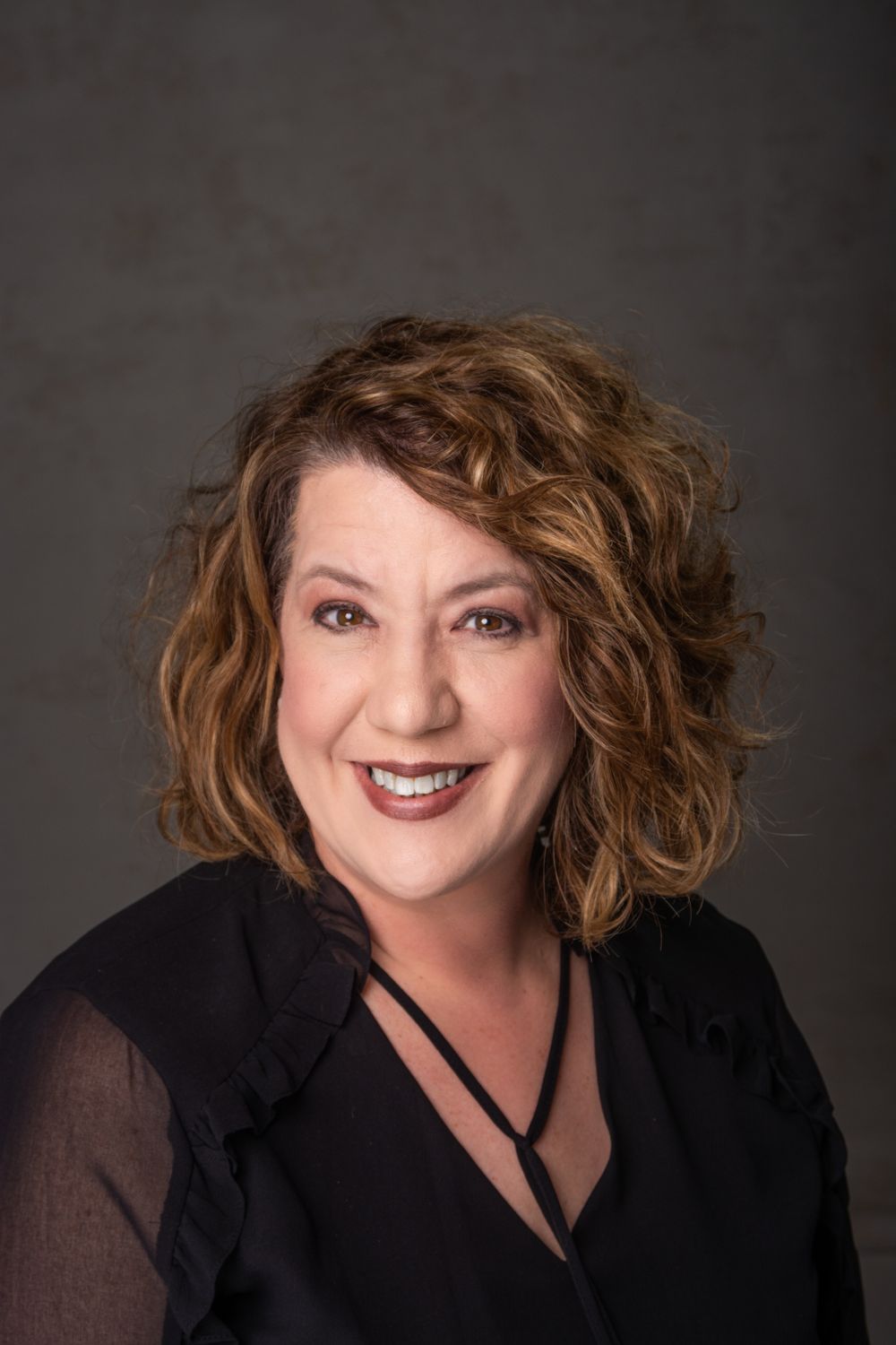 Headshot of woman over 50 with black shirt and big smile.