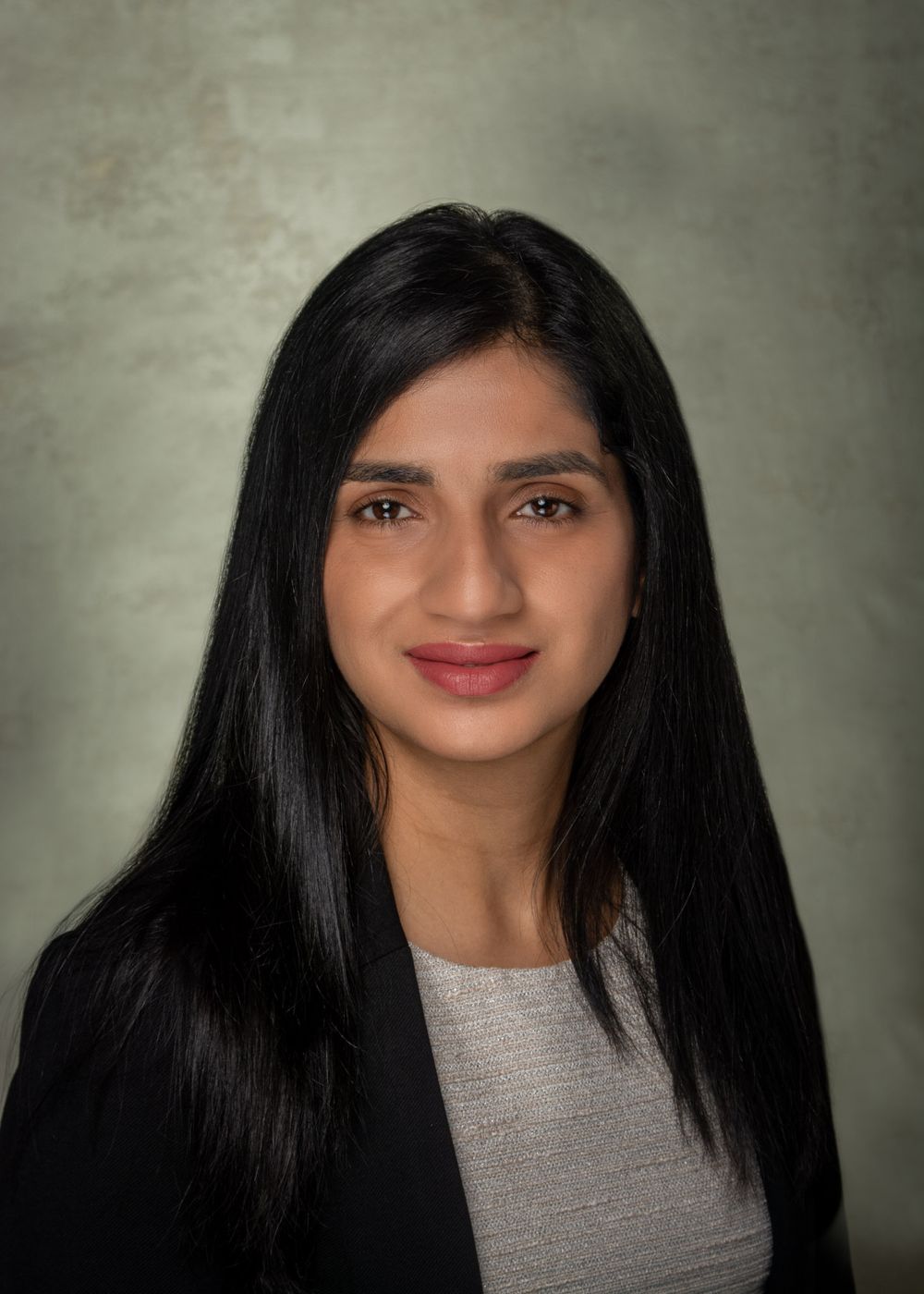 Business headshot of Indian woman in business suit and light colored top.