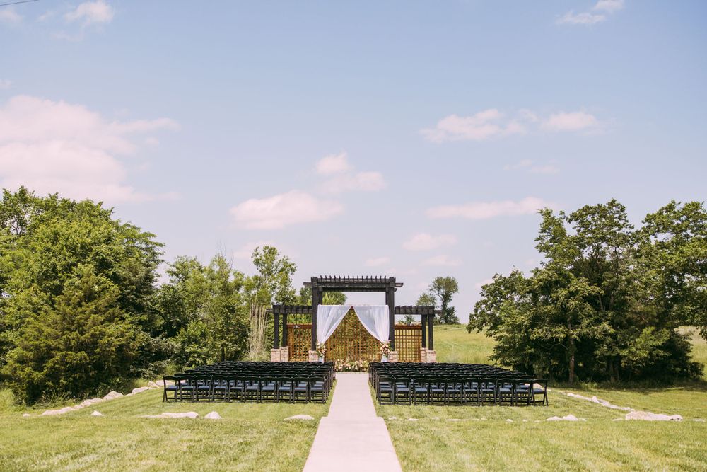 Outdoor wedding ceremony setup with wooden arch and white chairs on a scenic grassy hill.
