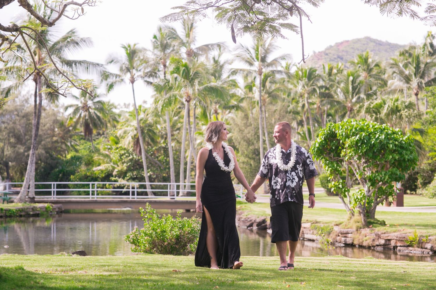 Couple holding hands walking through lush tropical garden with palm trees and pond in Hawaii.