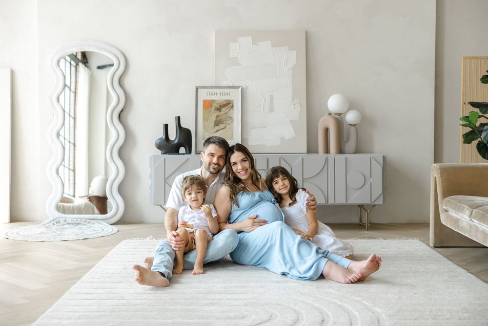 A family sits together on the floor of a modern, minimalist living room with white decor and natural light.