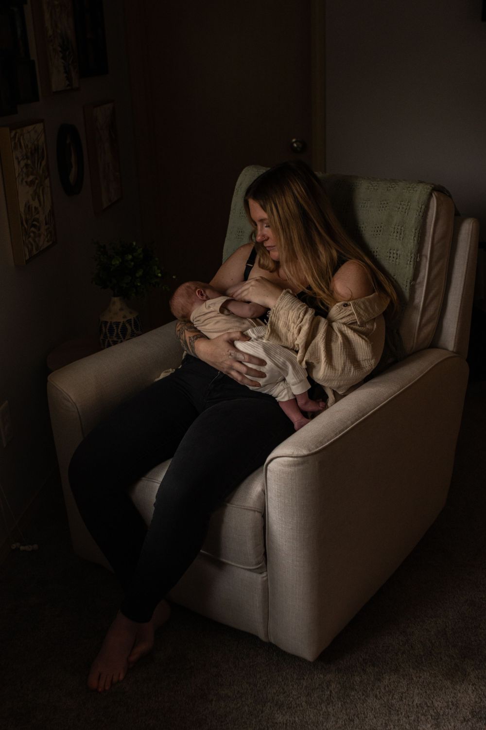 A new mom breastfeeds her newborn in a lounge chair by the light of the window