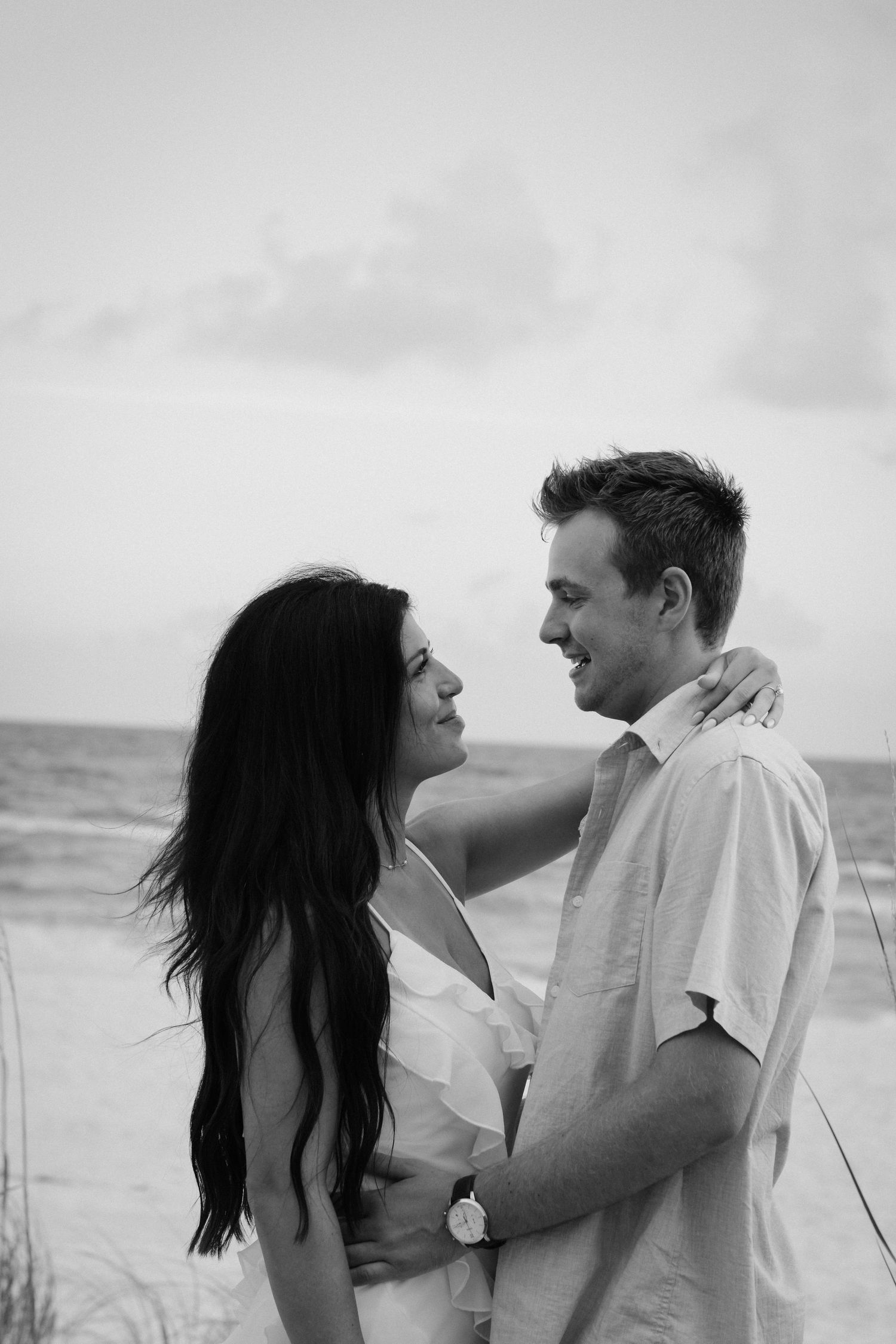 Romantic couple embraces on beach in black and white photography series.
