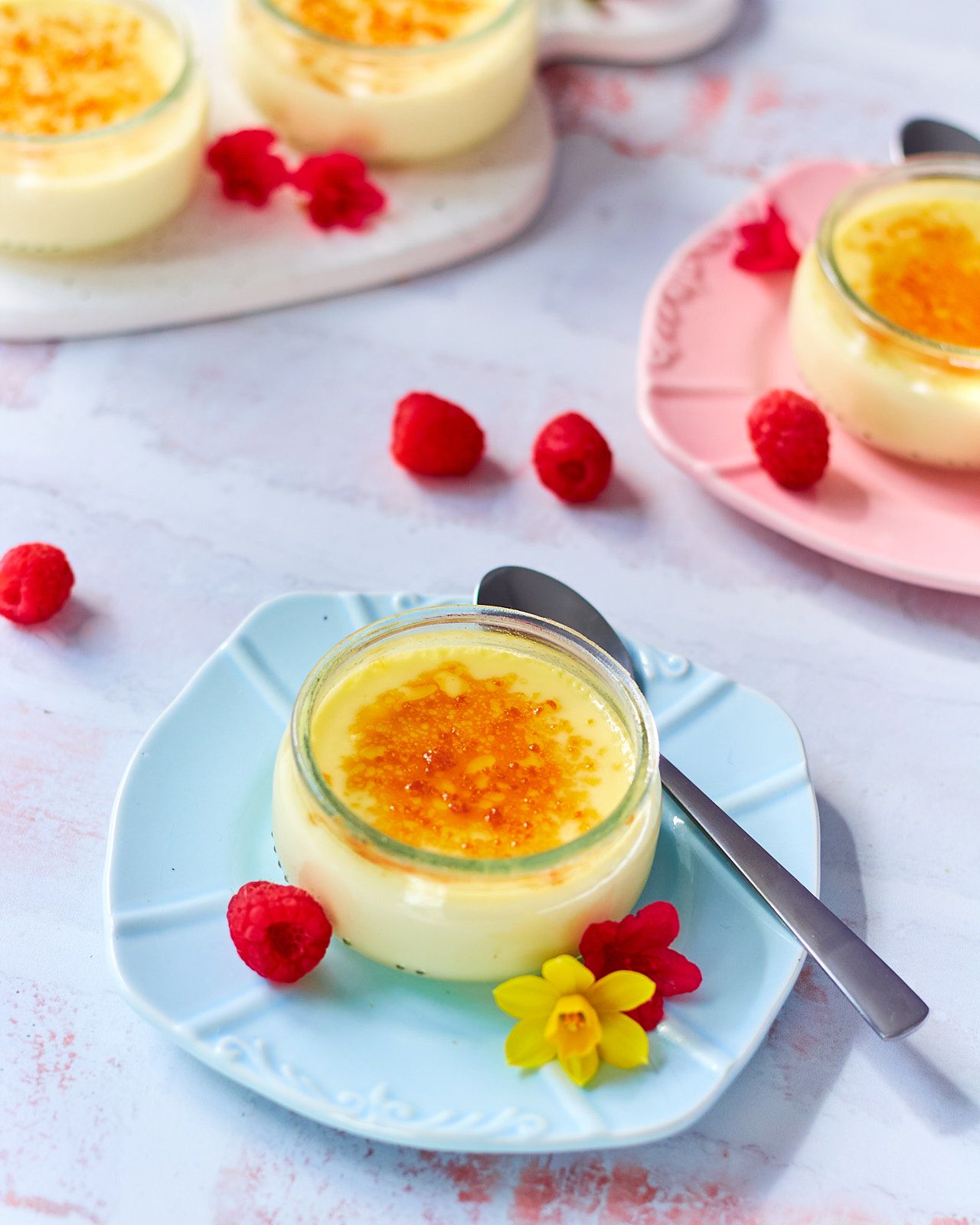Image of Creme brulee in a small Ramikin on a light blue plate with other jars of creme brulee in the back ground.