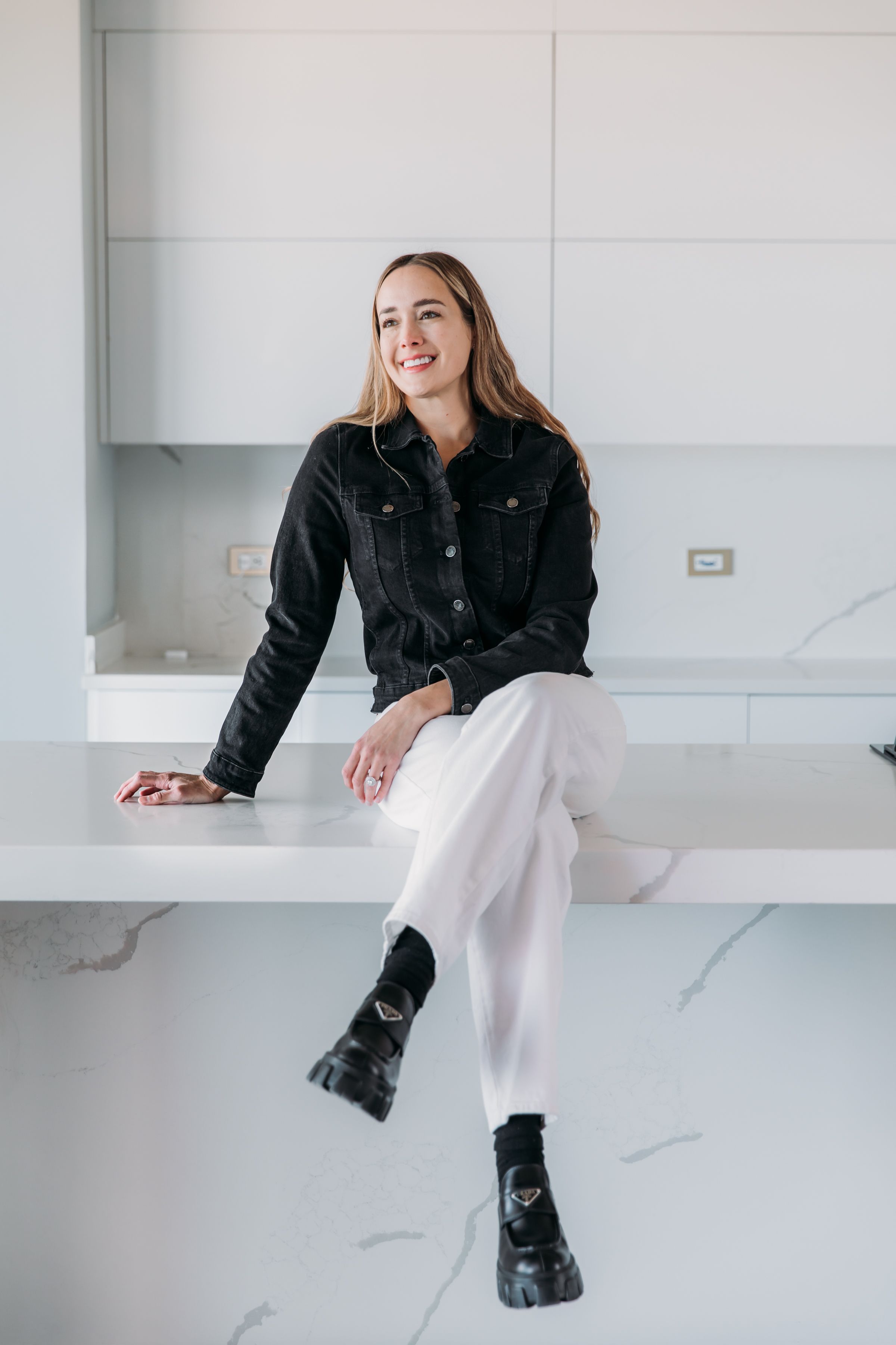 Casual portrait in black denim jacket and white pants on modern marble counter.