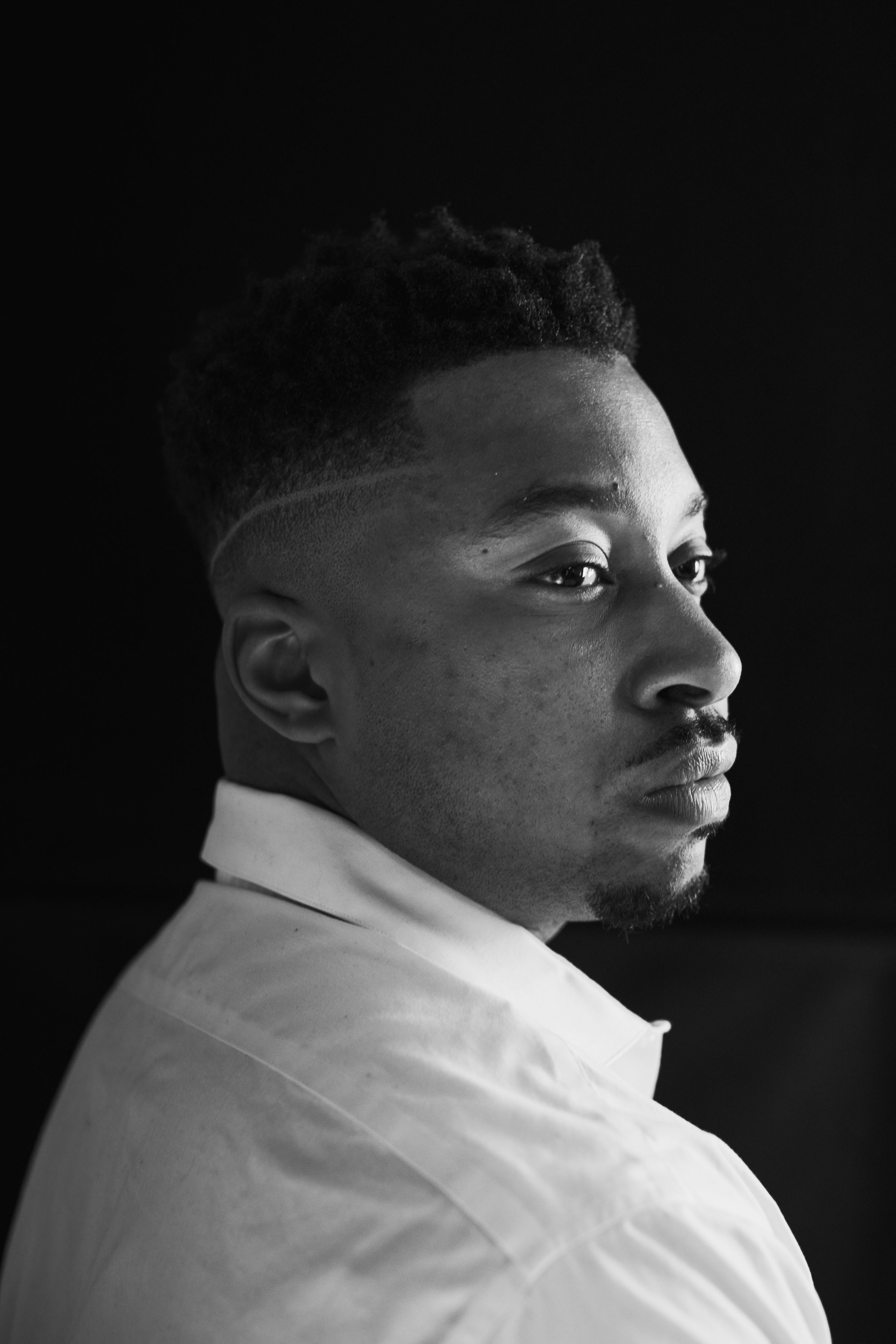 Black and white profile portrait of a person in white collar shirt against dark background.