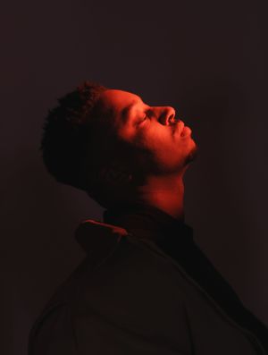 Dramatic red-lit profile portrait captured against a dark background in moody lighting.