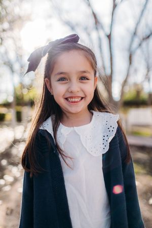 Young girl in navy coat smiling brightly in natural outdoor lighting.