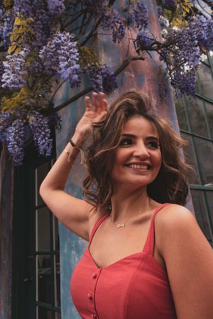 Joyful summer portrait under blooming wisteria with coral red tank top.