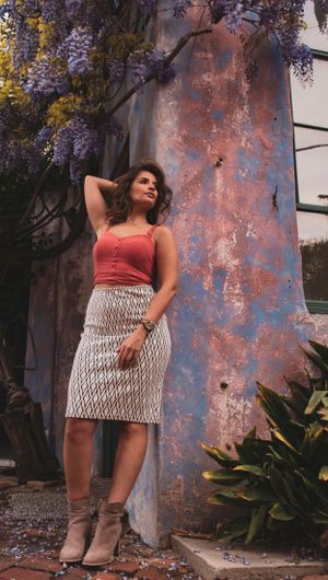 Fashion portrait with coral top and patterned skirt against textured wall with wisteria.
