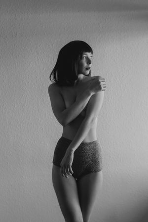 Artistic black and white photograph showing a minimalist pose against a plain wall.