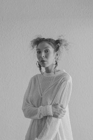 Black and white portrait of someone in a white sweater with messy buns and hoop earrings.