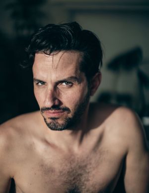 Dramatic close-up portrait showing a shirtless person in moody lighting.