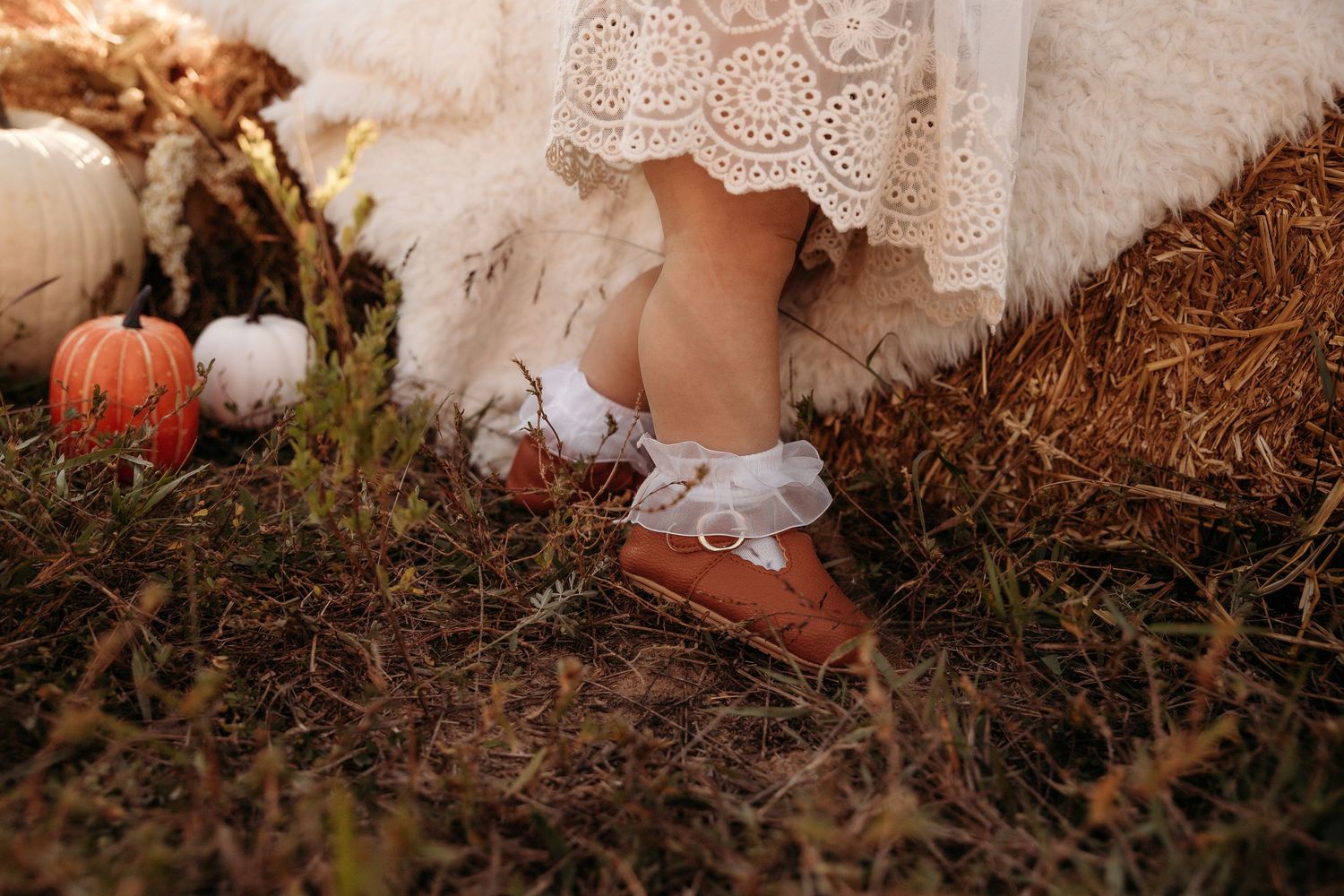 Close-up details of lace and delicate embroidery on white vintage-style dress against rustic backdrop.