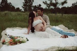 Two people sharing an intimate moment on a white blanket outdoors with scattered roses in the grass.