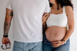 Cropped view of an expectant couple standing close together showing pregnant belly and tattoos.