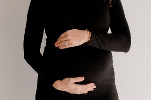 Close up of hands cradling a pregnant belly wearing a black long sleeve dress against a white background.