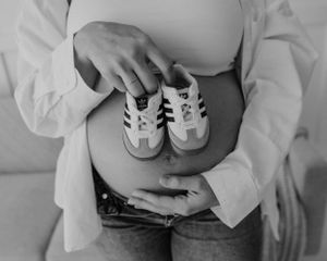 Tiny black and white baby shoes held against a pregnant belly in black and white photography.