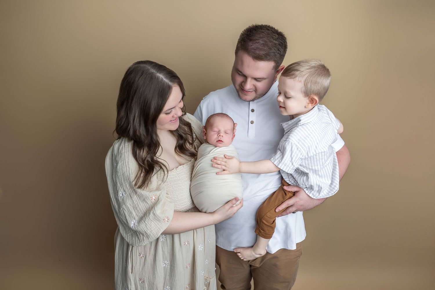 Natural family portrait in muted tones showing parents with their children sitting together on white surface.