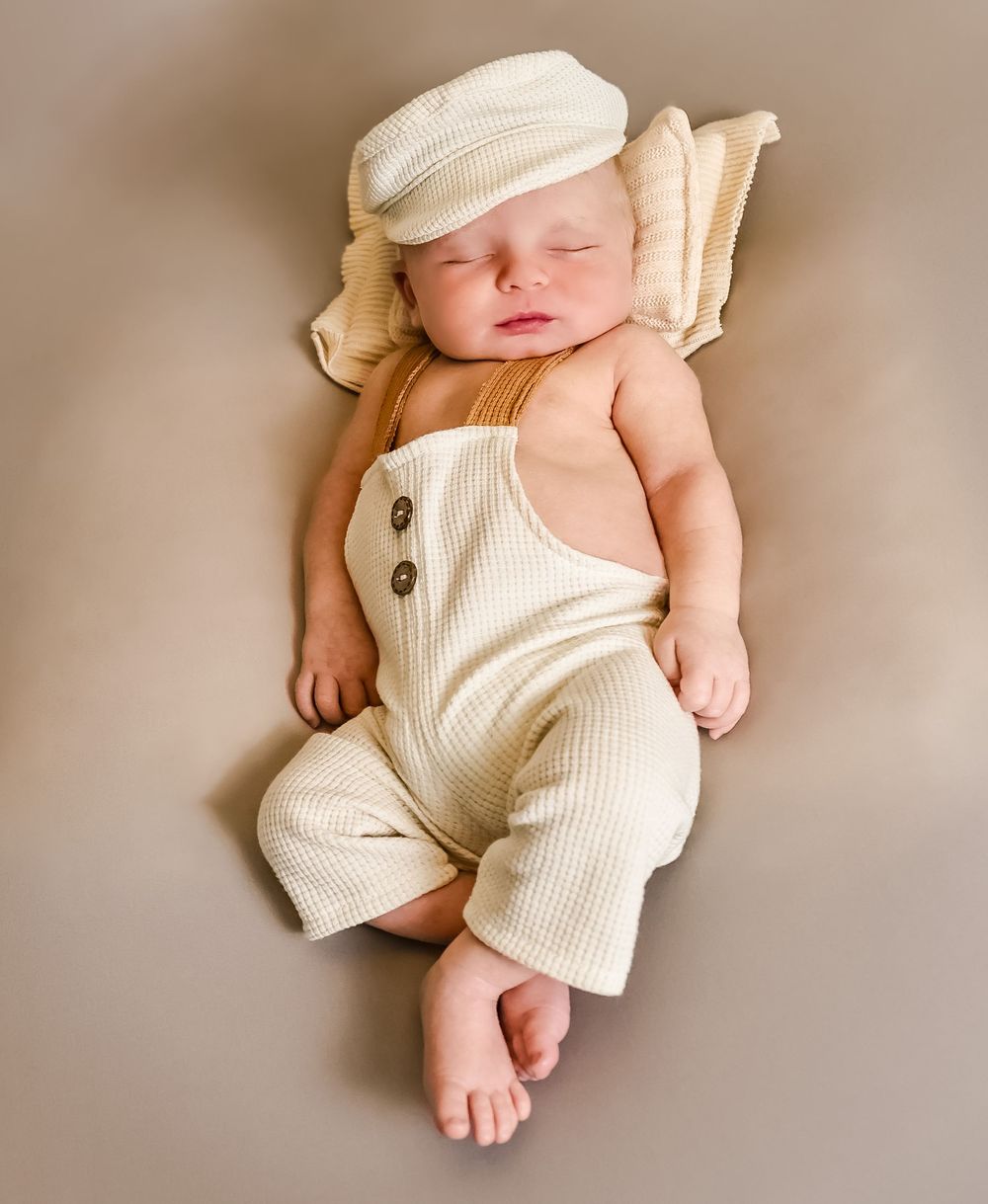 Newborn baby wearing cream-colored ribbed outfit lying on neutral background.