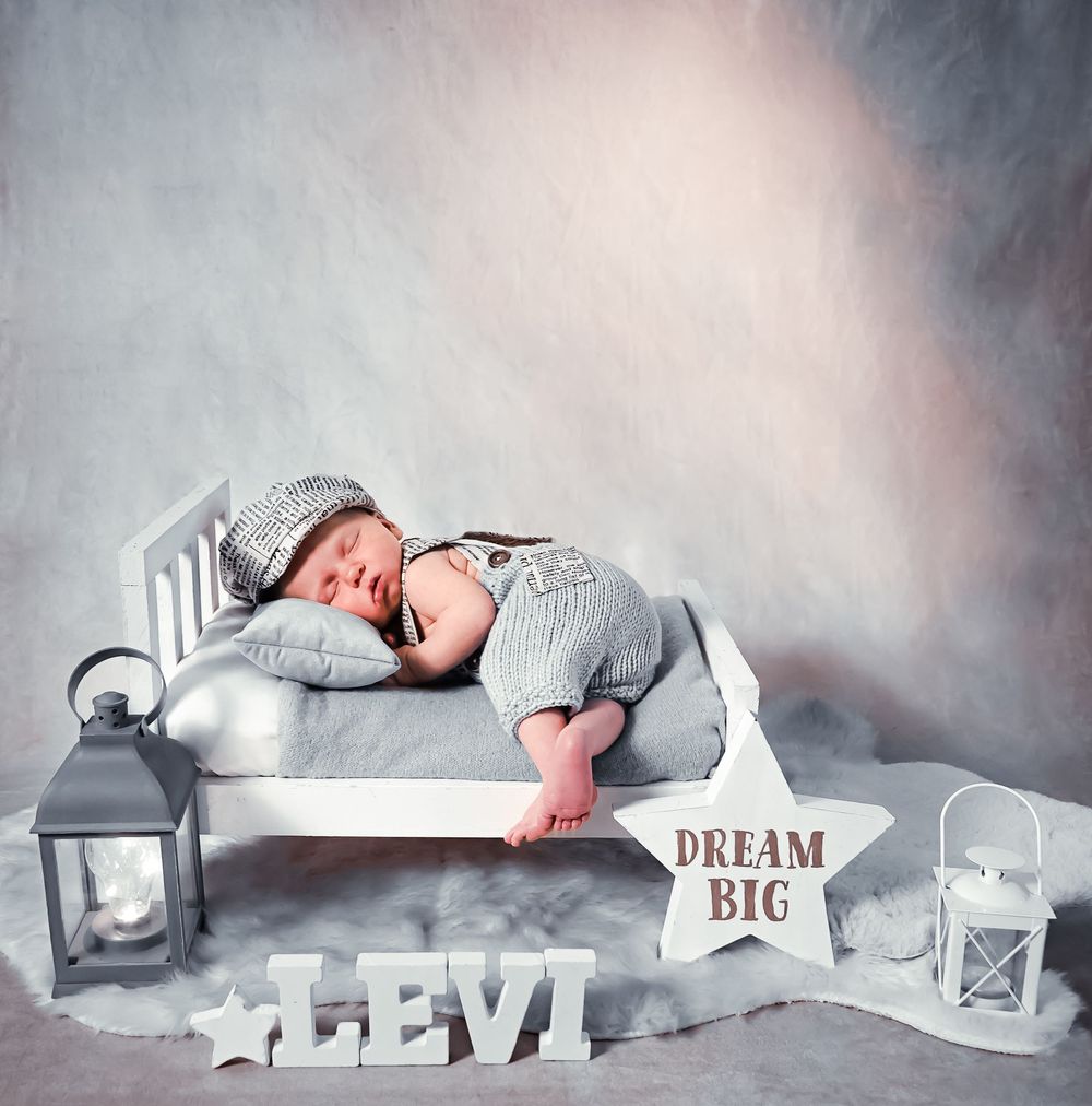 Sleeping baby in gray outfit surrounded by dreamy star decorations and lanterns.