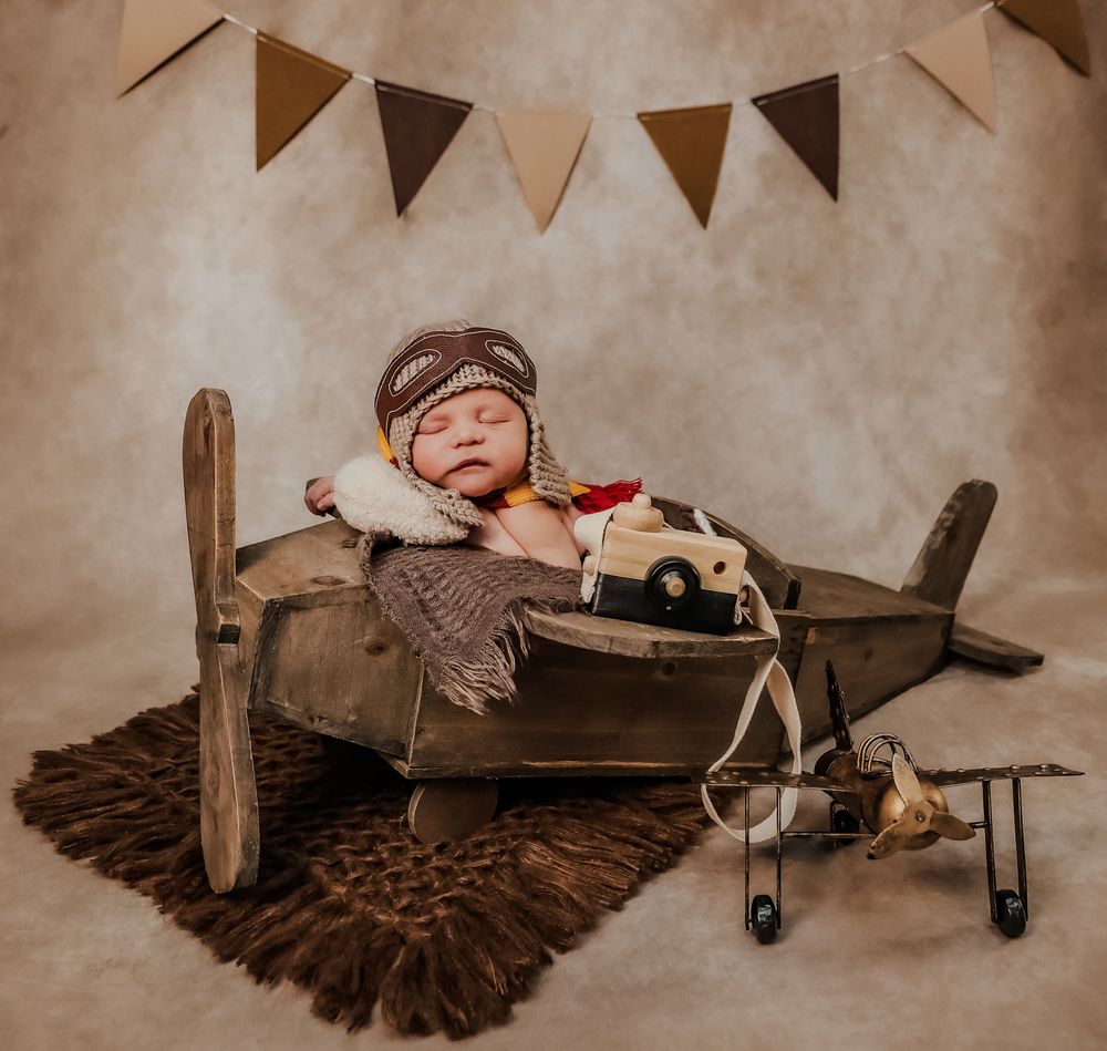 Vintage-themed baby photo with toy airplane and brown feathered wings on sepia background.