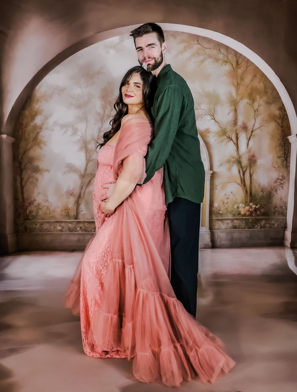 Couple embracing in formal wear against vintage painted wall backdrop.