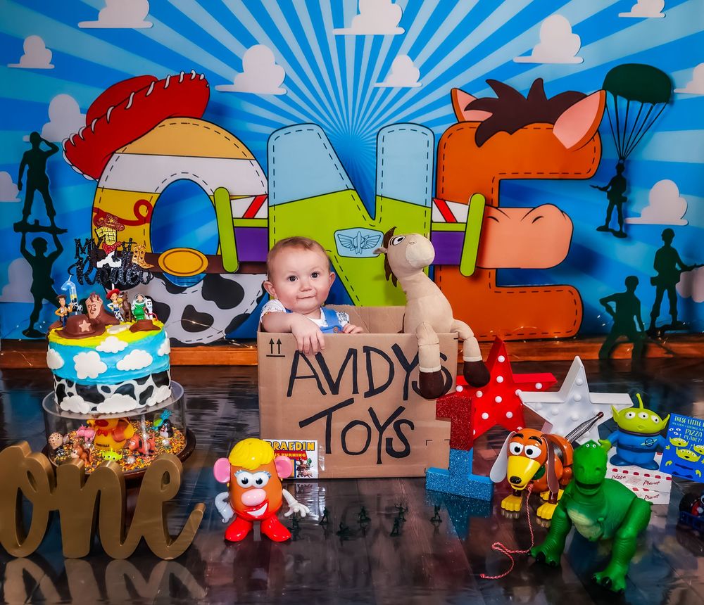 Colorful toy-themed party backdrop with blue sunburst pattern and cartoon decorations.