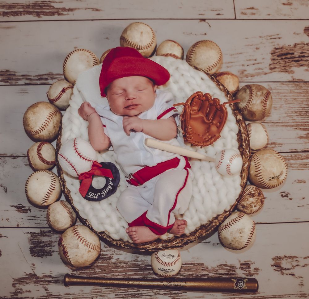Baseball-themed newborn photo shoot with baby surrounded by baseballs on rustic wood background.