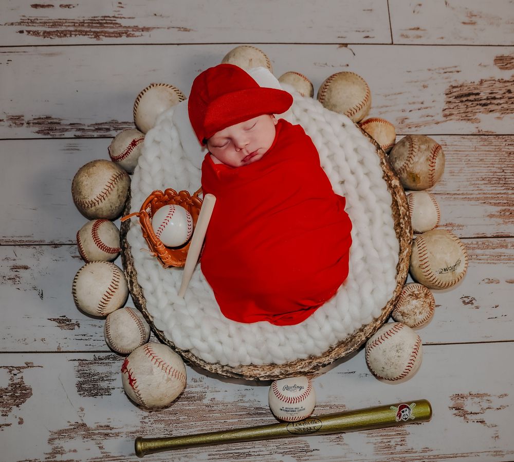 Baseball-themed baby portrait with red outfit and vintage baseballs on distressed wood surface.