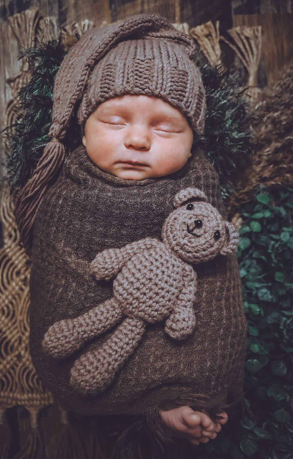 Baby wrapped in brown knit blanket with matching teddy bear accessory in outdoor setting.