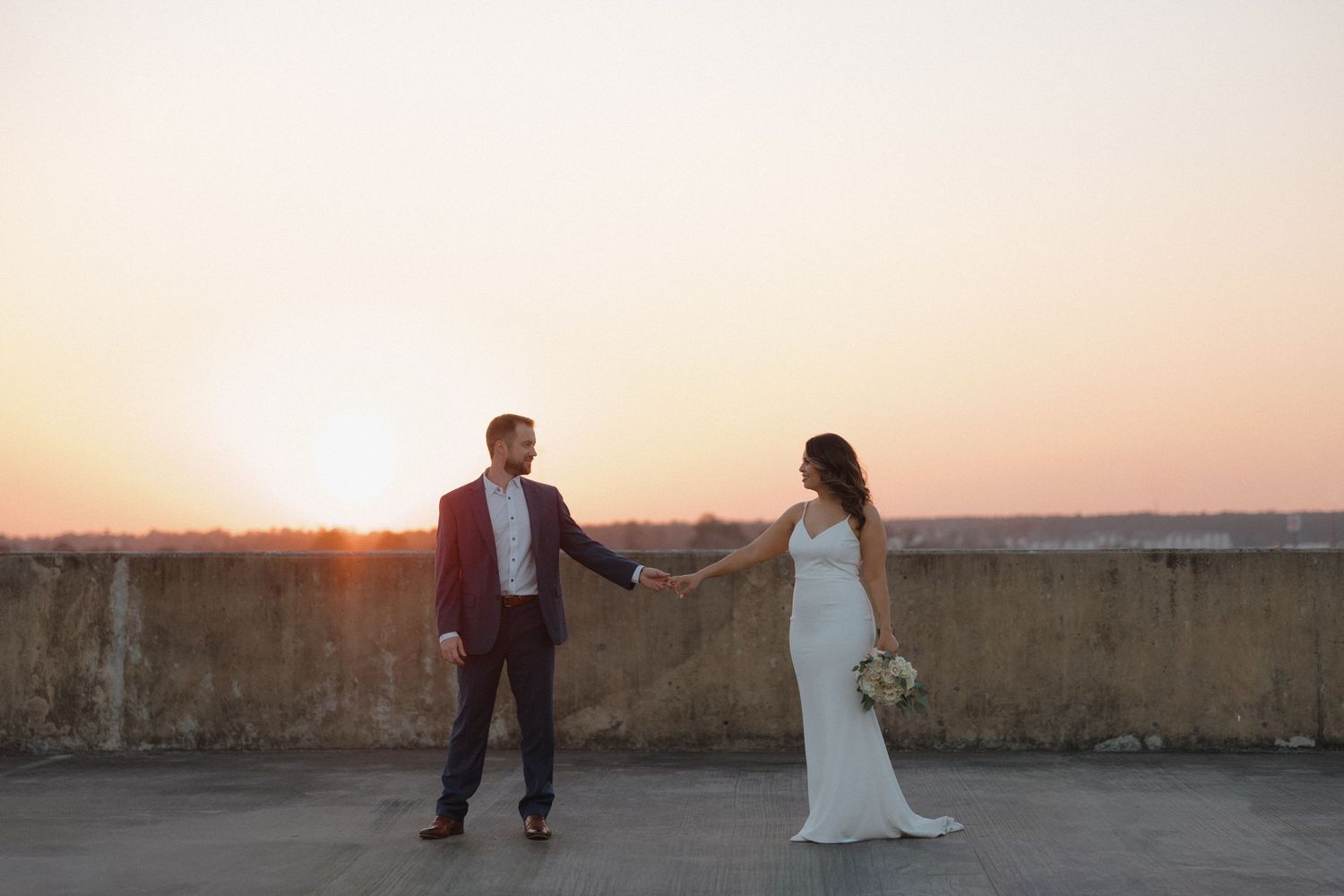 A glamorous couple poses beside a classic light blue car on their wedding day.