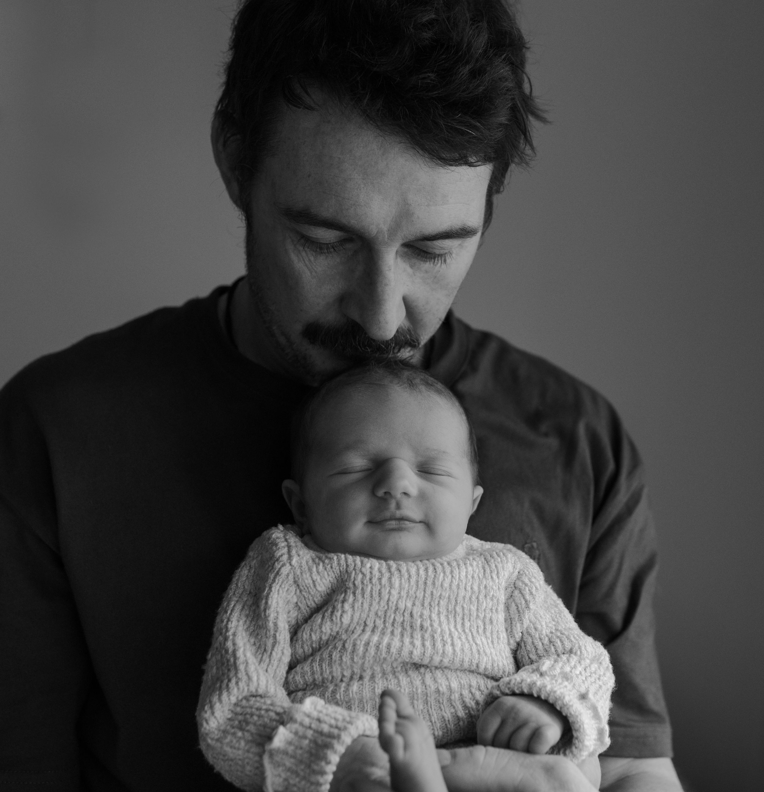 A series of black and white photos showing a parent and baby in tender intimate moments of bonding and affection.