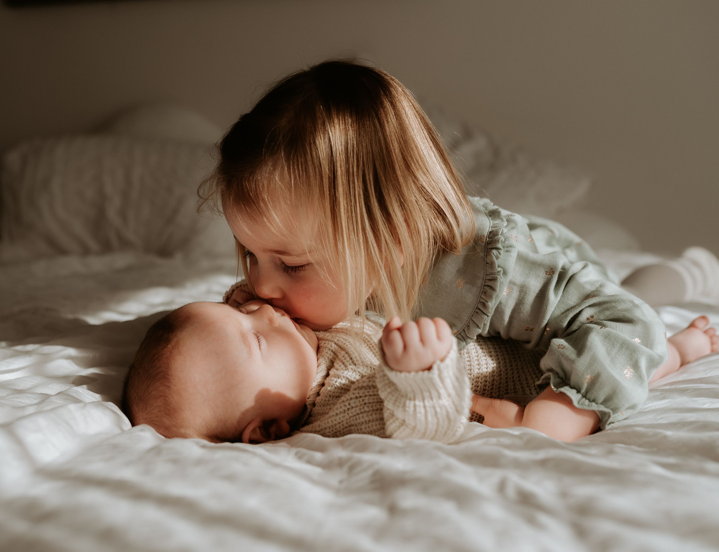 Two young children share a sweet moment together while laying on white bedding.
