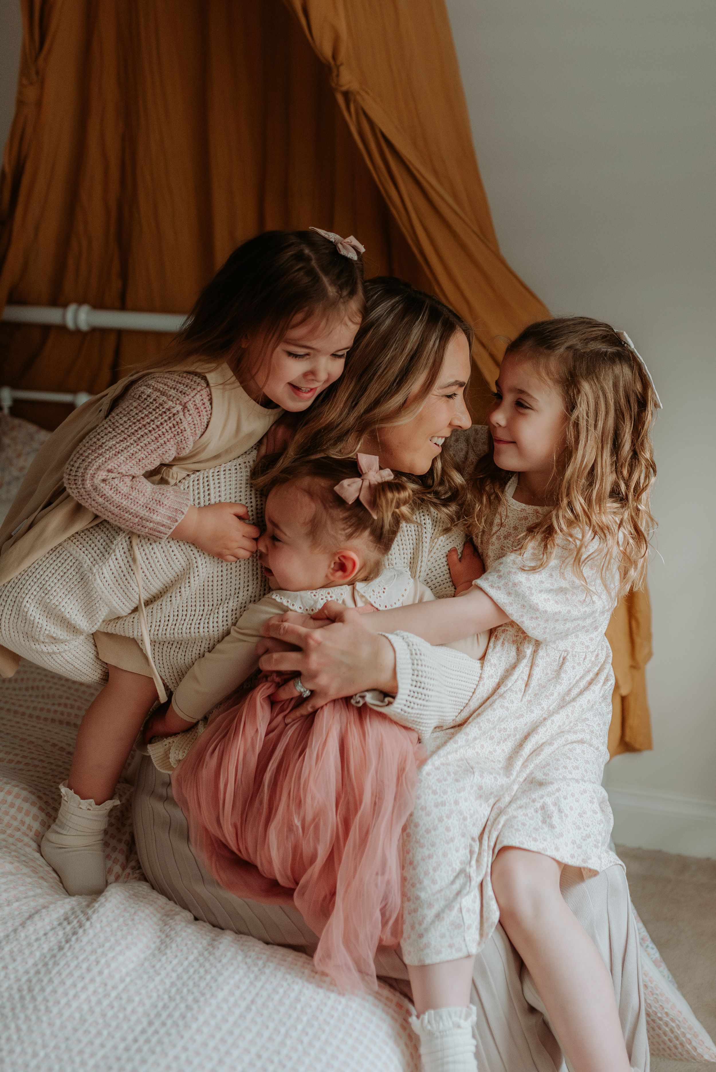 A tender family moment captured in a series of intimate photos showing affectionate embraces on a bed with soft lighting.