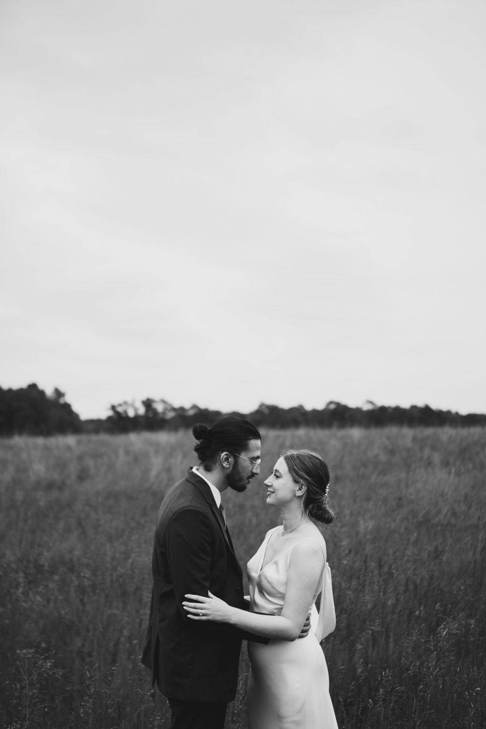 A black and white wedding portrait of a couple in formal attire standing in a field.
