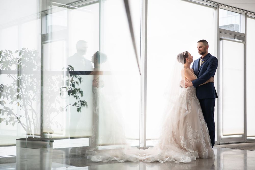 A couple shares an intimate moment in a bright modern space with floor-to-ceiling windows.