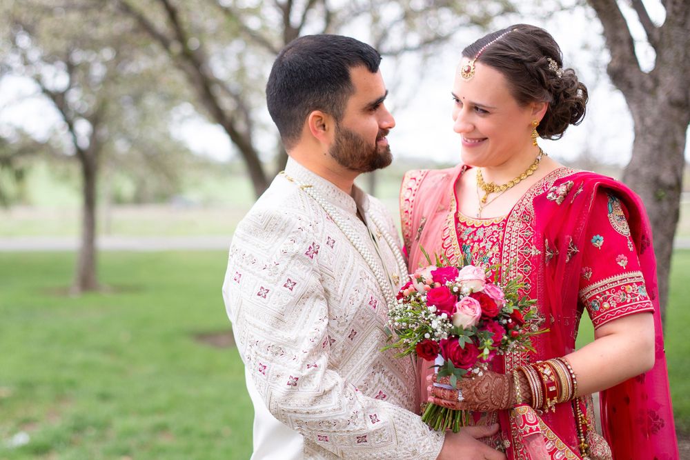 A couple in traditional Indian wedding attire shares a tender moment in a spring garden setting.
