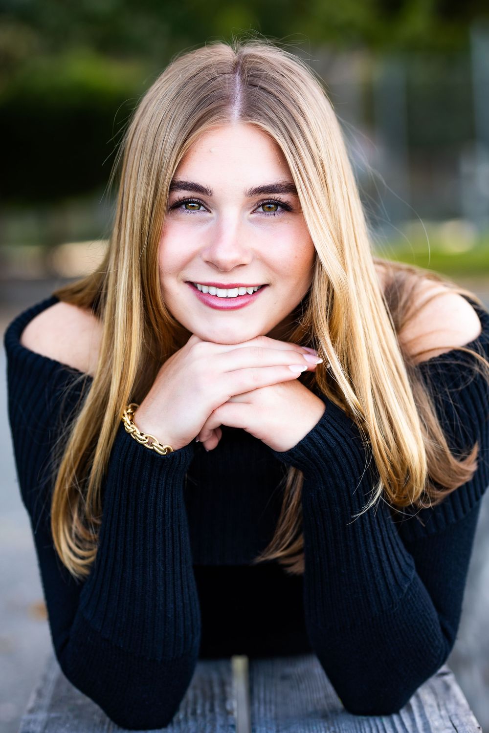 Portrait of blonde girl in black sweater resting chin on hands outdoors.
