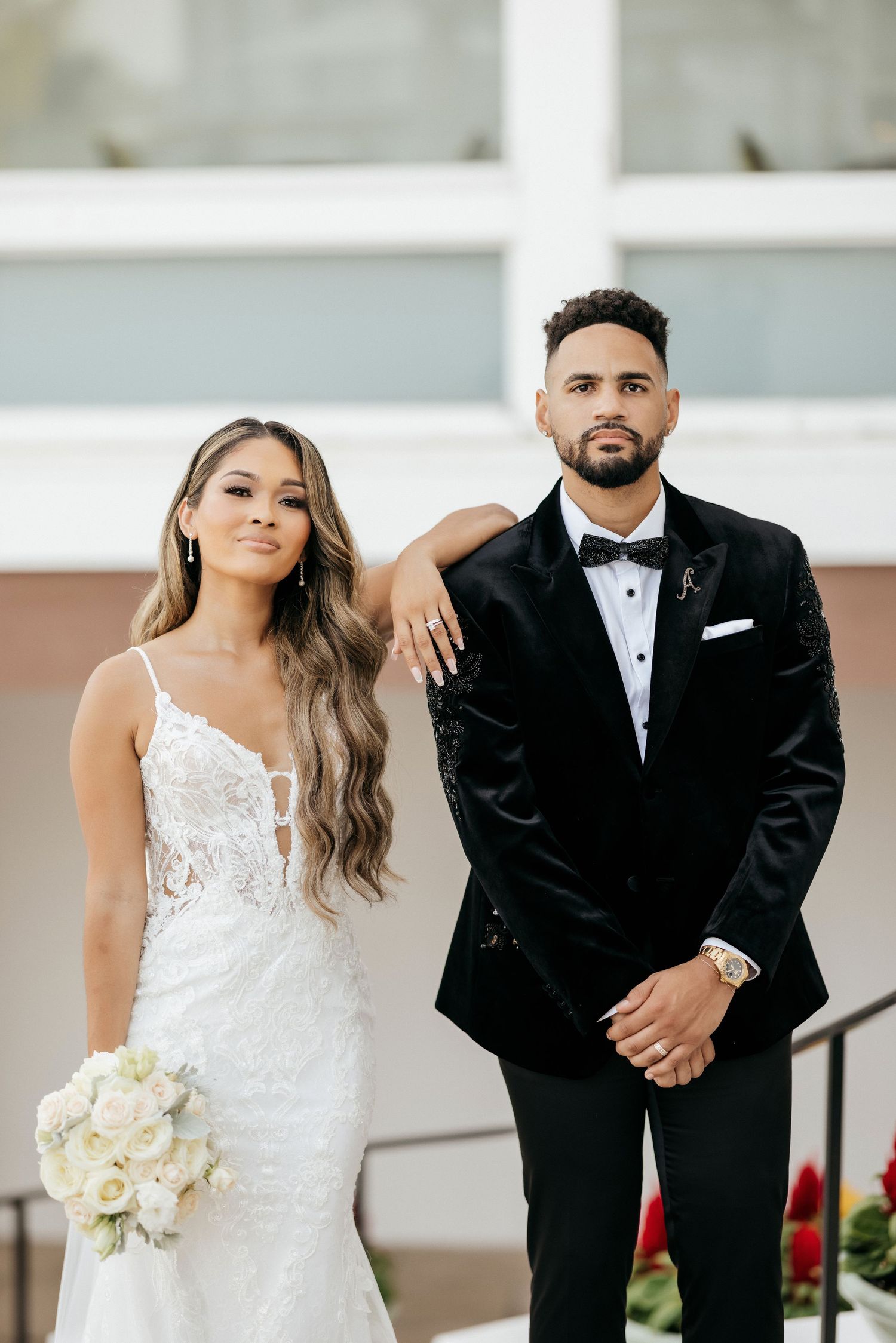 Elegant bride in lace gown and groom in velvet tuxedo pose together on wedding day.