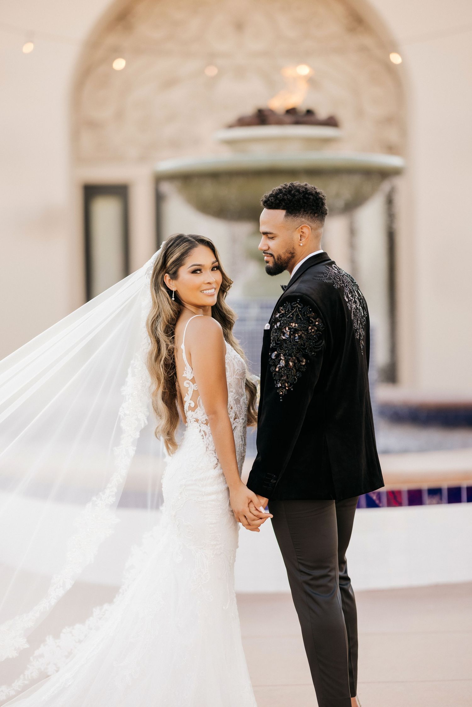 Romantic wedding portrait of couple with flowing veil against arched architecture.