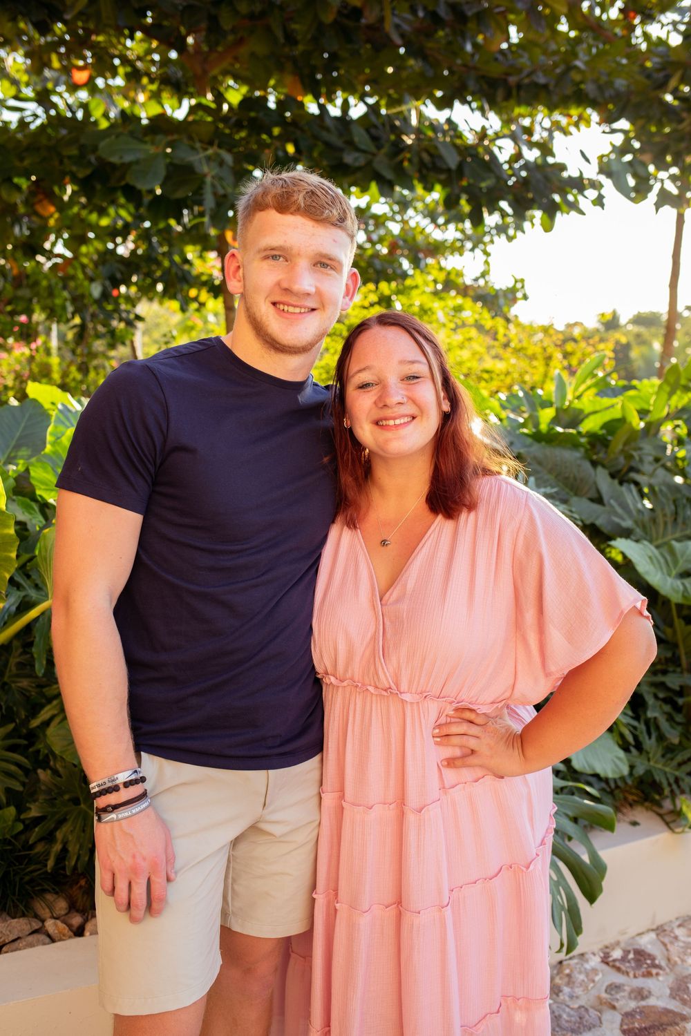 Siblings poses outdoors in coordinated outfits with a navy shirt and khaki shorts and a flowing pink dress.