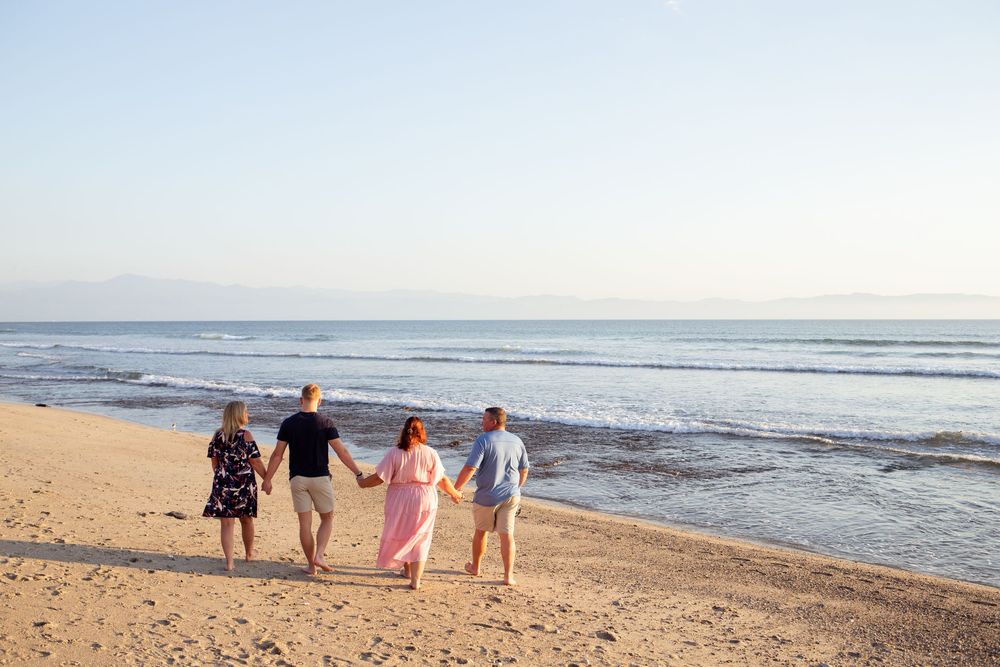 Family portrait of people walking along a scenic beach shoreline with rolling waves and ocean views at sunset.