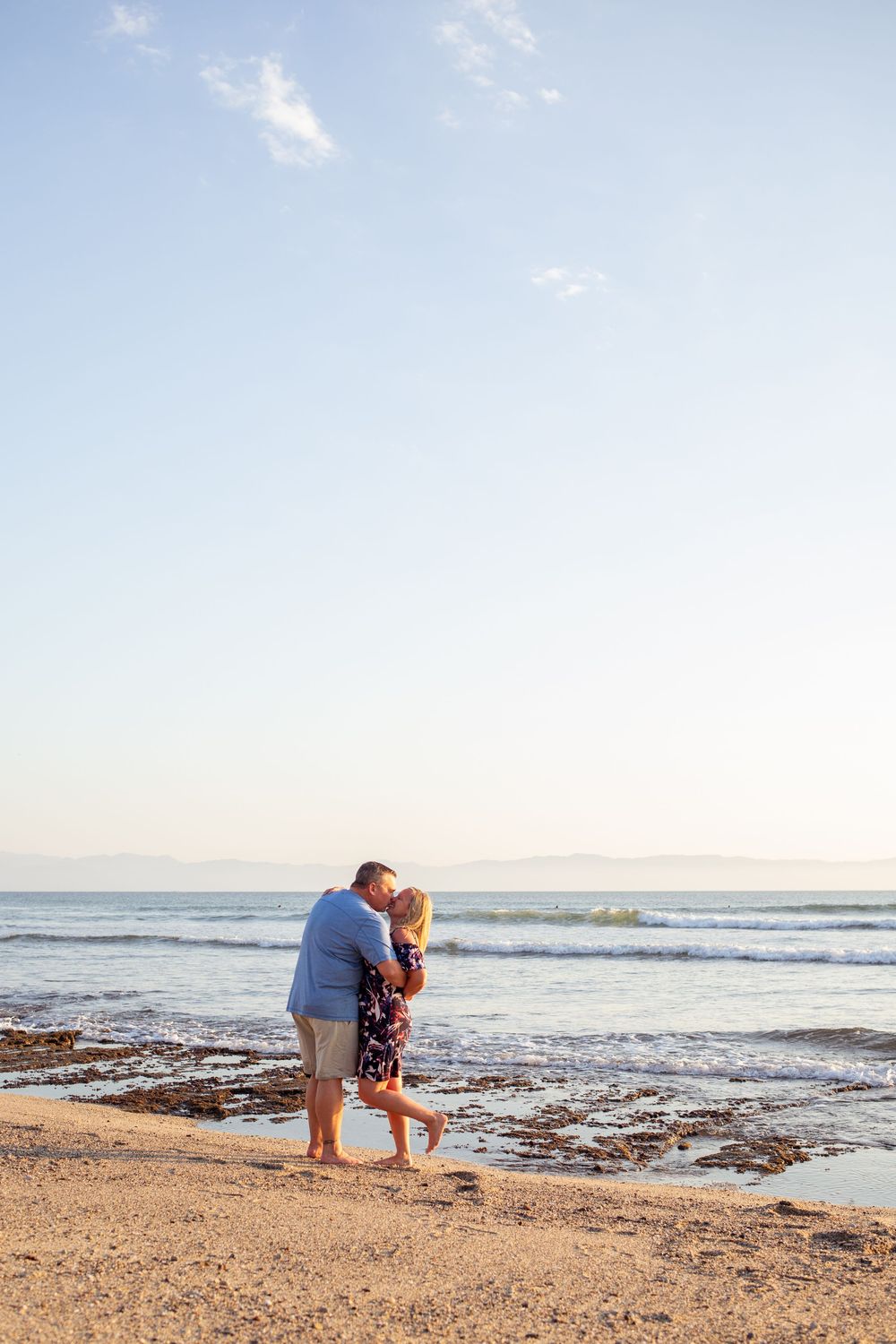 Two people in an embrace at sunset while waves gently roll onto the sandy shore.